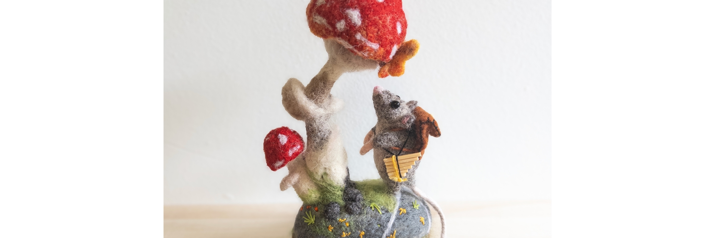 Small figurine of a mouse with a basket and mushrooms on a rock against a white background