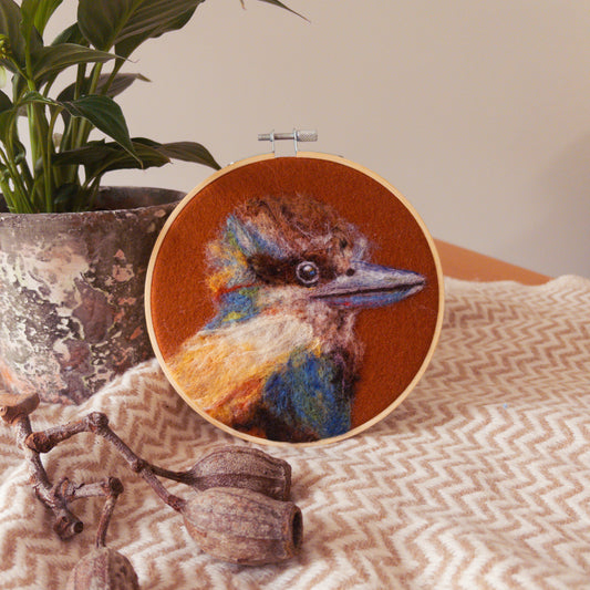 Embroidery hoop with a colorful bird design on a textured surface with a plant in the background
