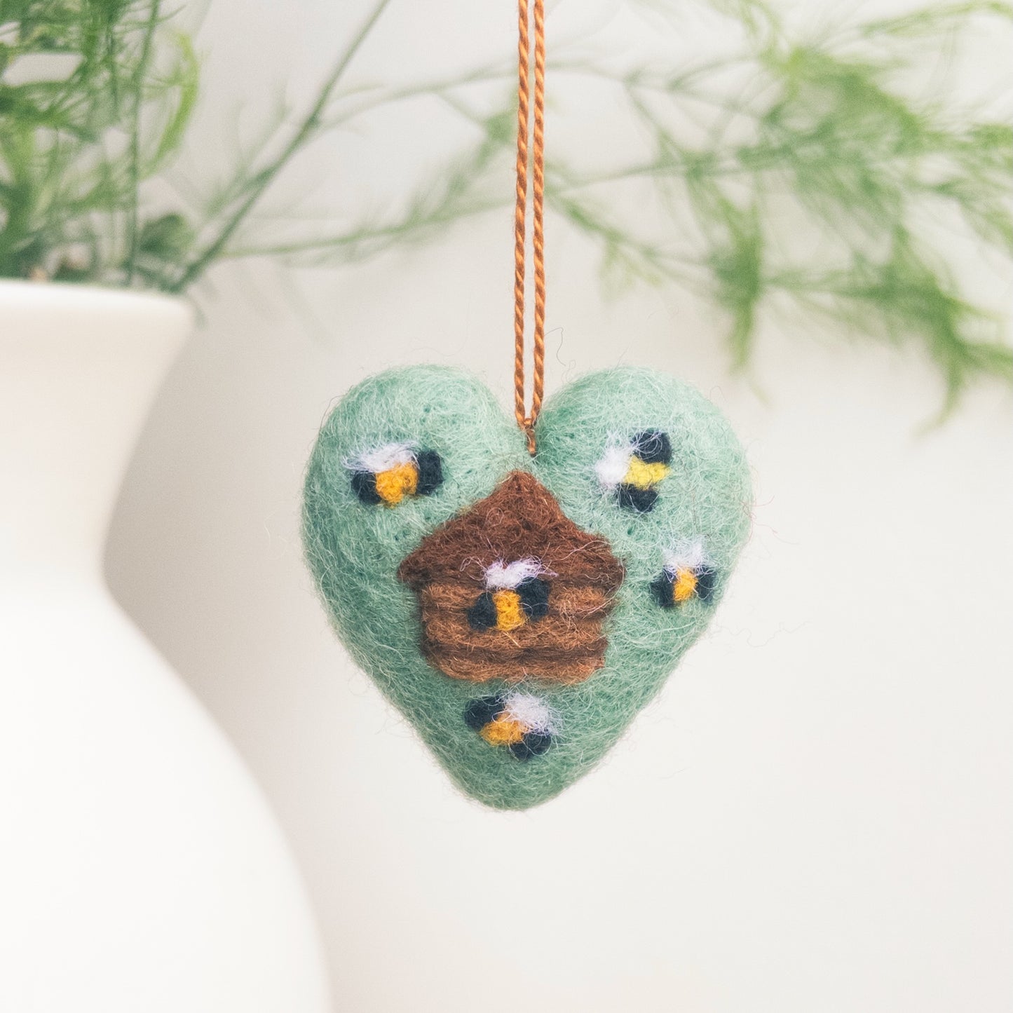 Heart-shaped felt ornament with birds and a nest, hanging against a white background.