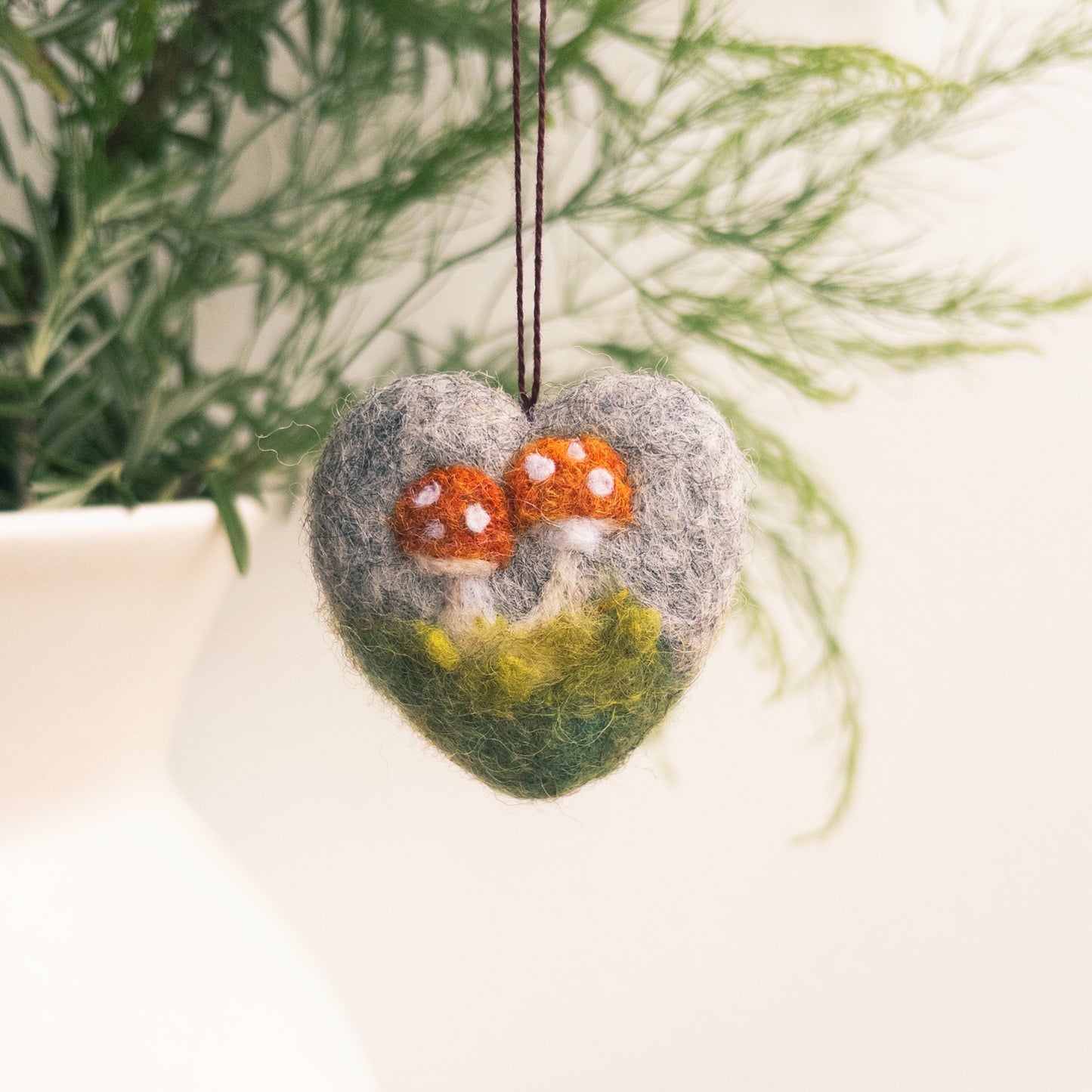 Heart-shaped felt ornament with mushrooms hanging against a natural background
