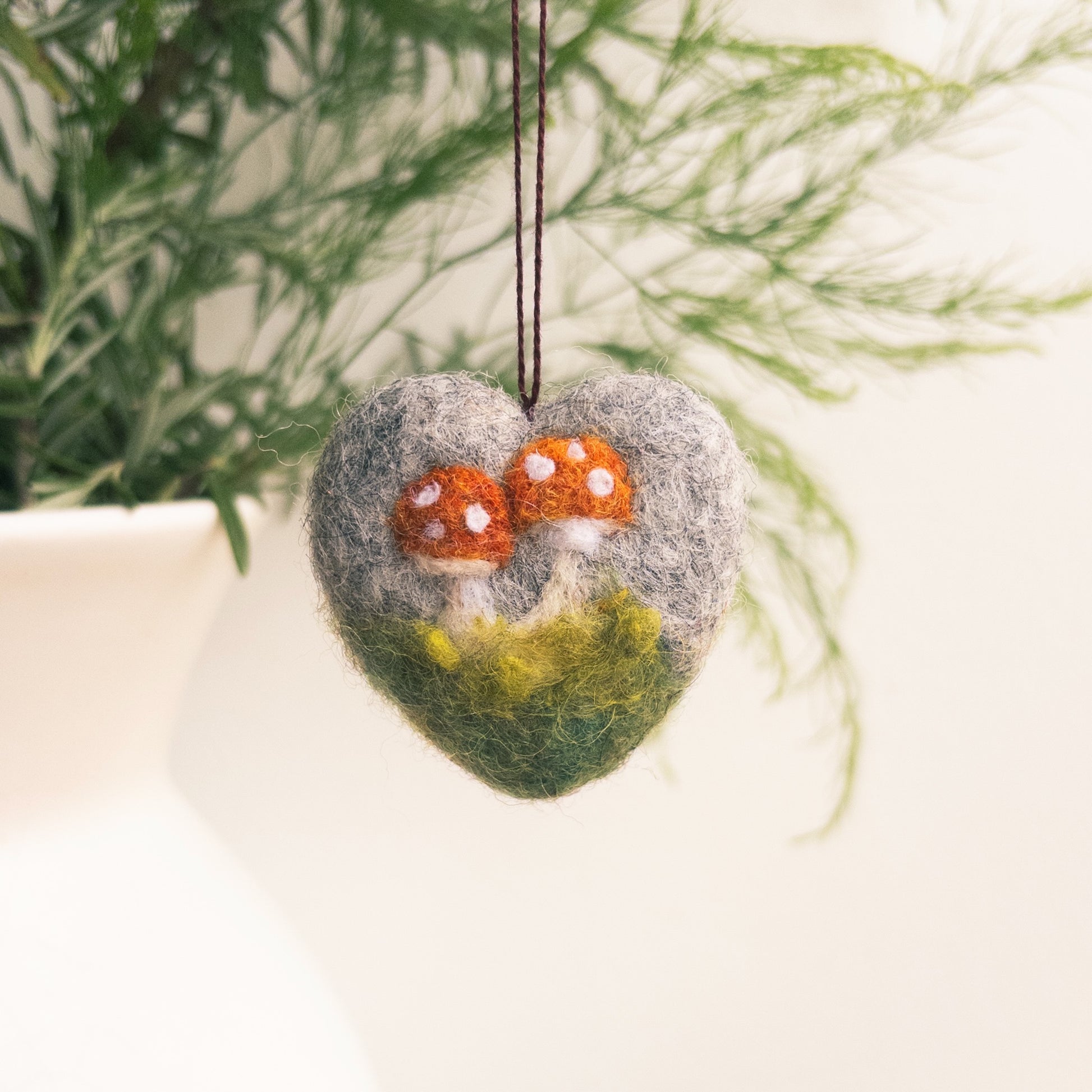 Heart-shaped felt ornament with mushrooms hanging against a natural background